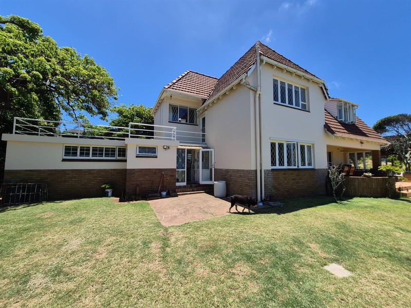 Rear view of a double-story residence featuring a tiled roof, brick and plaster facade, and an elevated balcony area overlooking the garden.