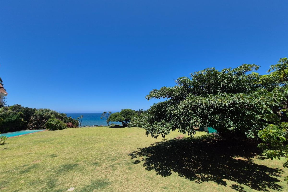 Expansive garden area featuring a well-maintained lawn, mature trees, and a scenic ocean view, providing a tranquil outdoor setting.