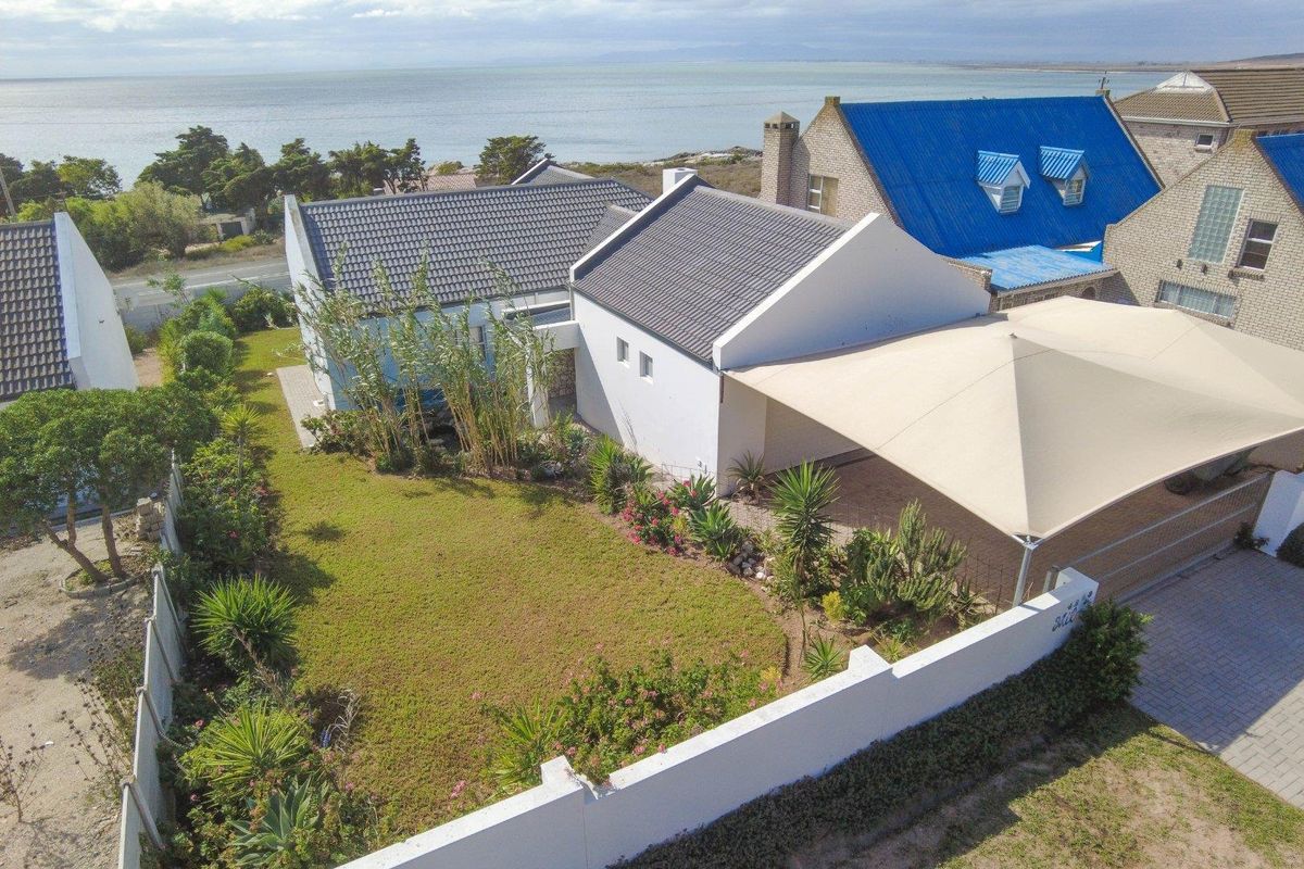Aerial view of a coastal property featuring a well-maintained garden, paved driveway with a shade sail, and proximity to the ocean.