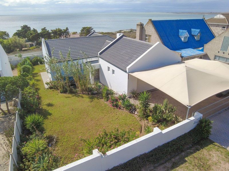 Aerial view of a coastal property featuring a well-maintained garden, paved driveway with a shade sail, and proximity to the ocean.