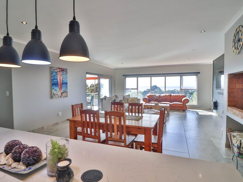 Spacious open-plan living and dining area featuring large format floor tiles, a brick fireplace, and seamless access to an outdoor patio with scenic views.