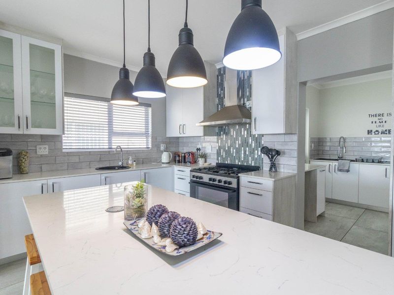 Modern kitchen featuring a large quartz island, gas stove with extractor fan, tiled backsplash, and ample built-in cabinetry, with an adjacent scullery area.