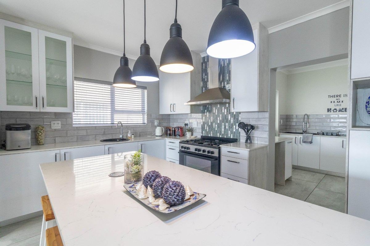 Modern kitchen featuring a large quartz island, gas stove with extractor fan, tiled backsplash, and ample built-in cabinetry, with an adjacent scullery area.