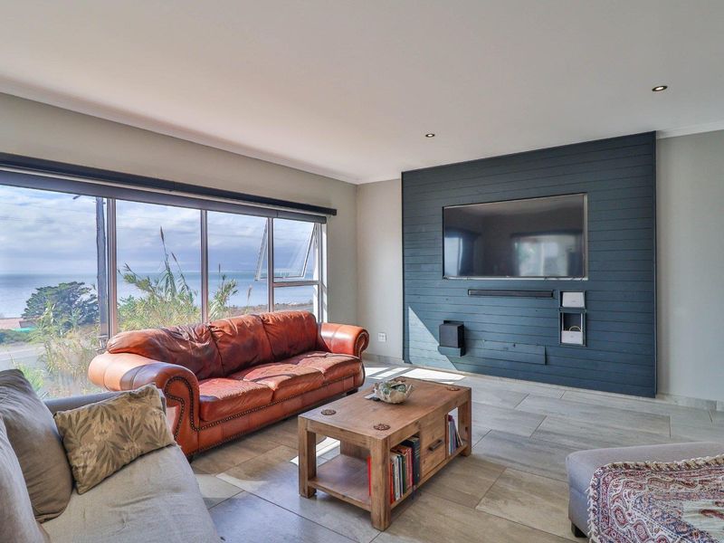 Spacious living room featuring large format floor tiles, a striking dark timber-clad feature wall, and expansive windows offering scenic coastal views.