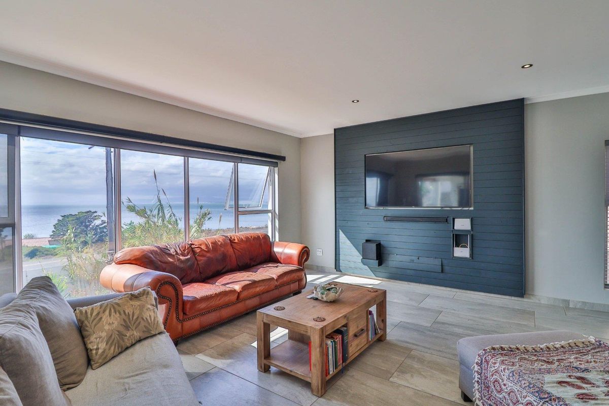 Spacious living room featuring large format floor tiles, a striking dark timber-clad feature wall, and expansive windows offering scenic coastal views.