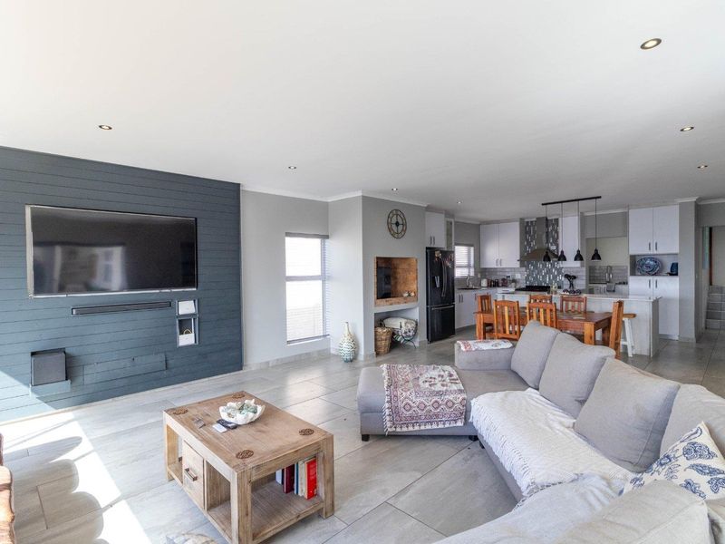 Spacious open-plan living area featuring a modern kitchen with island, tiled flooring, recessed lighting, and a contemporary feature wall.