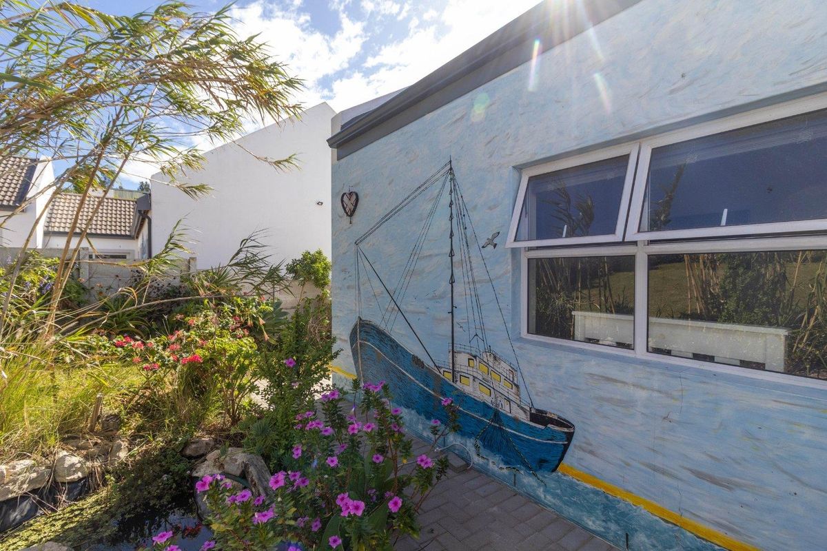 A rear exterior view of the property featuring a paved walkway alongside a wall decorated with a nautical mural and an awning window.