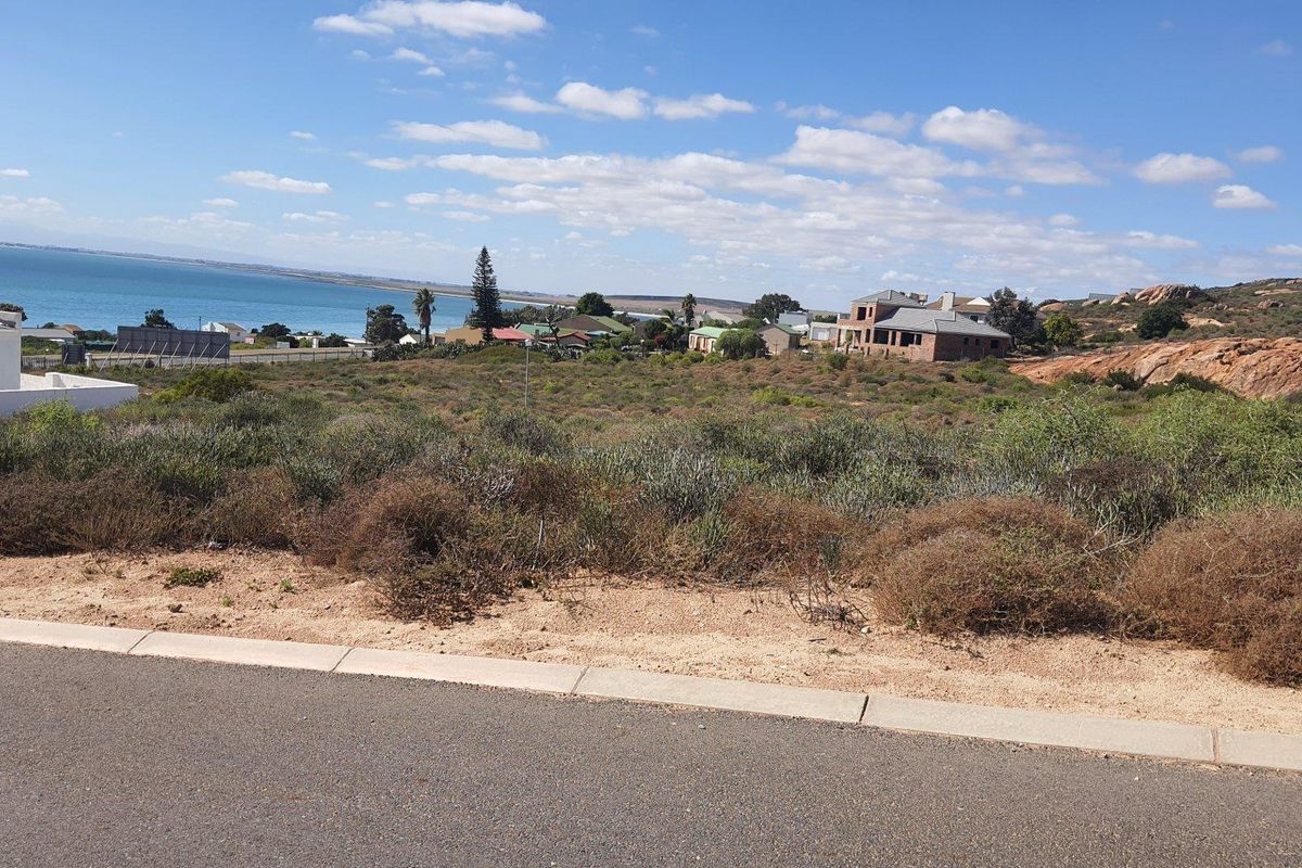 A vacant residential plot featuring natural coastal vegetation and scenic ocean views, situated in a developed neighborhood with paved street access.