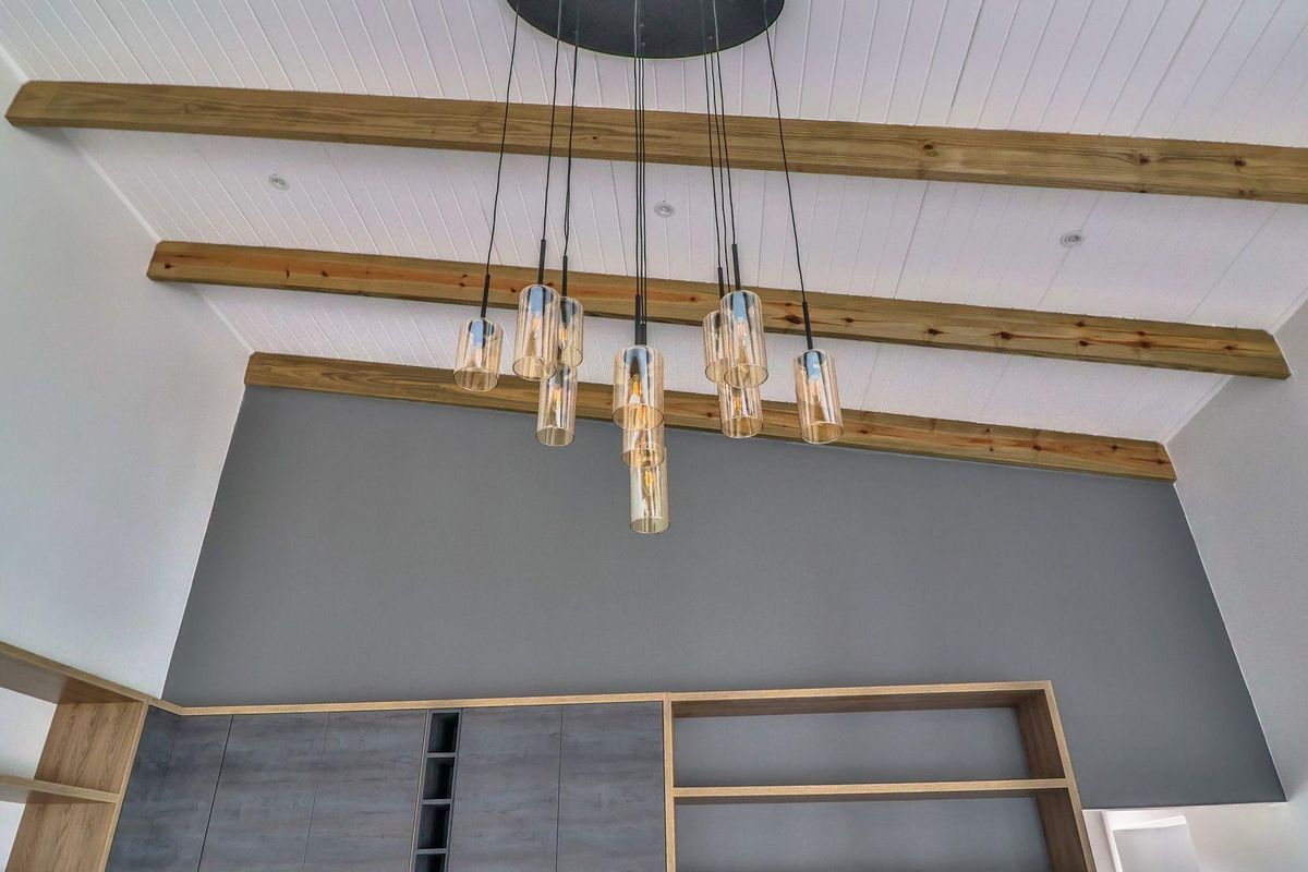 A modern living space featuring high ceilings with exposed timber beams, stylish pendant lighting, and custom built-in cabinetry with integrated shelving.