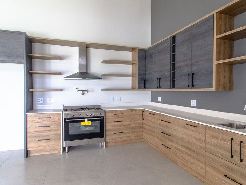 Modern kitchen featuring two-tone cabinetry, stone countertops, stainless steel gas stove, extractor fan, and a convenient pot filler faucet.