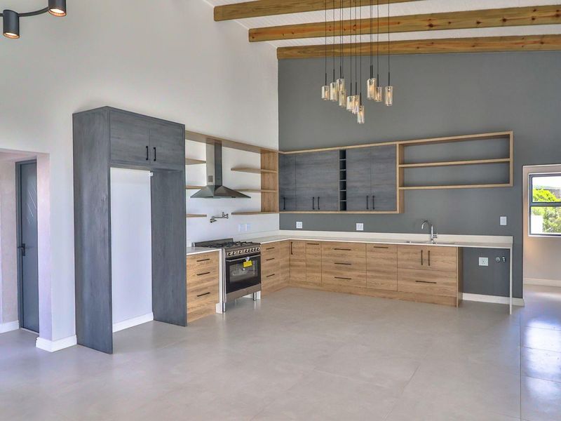Modern open-plan kitchen featuring two-tone cabinetry, timber shelving, gas stove, extractor fan, and exposed timber ceiling beams in a spacious, light-filled area.