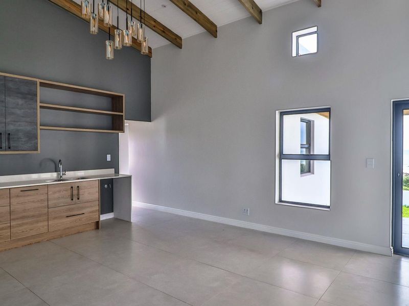 Modern open-plan living area featuring high ceilings with exposed timber beams, sleek built-in cabinetry, tiled floors, and direct access to an outdoor patio.