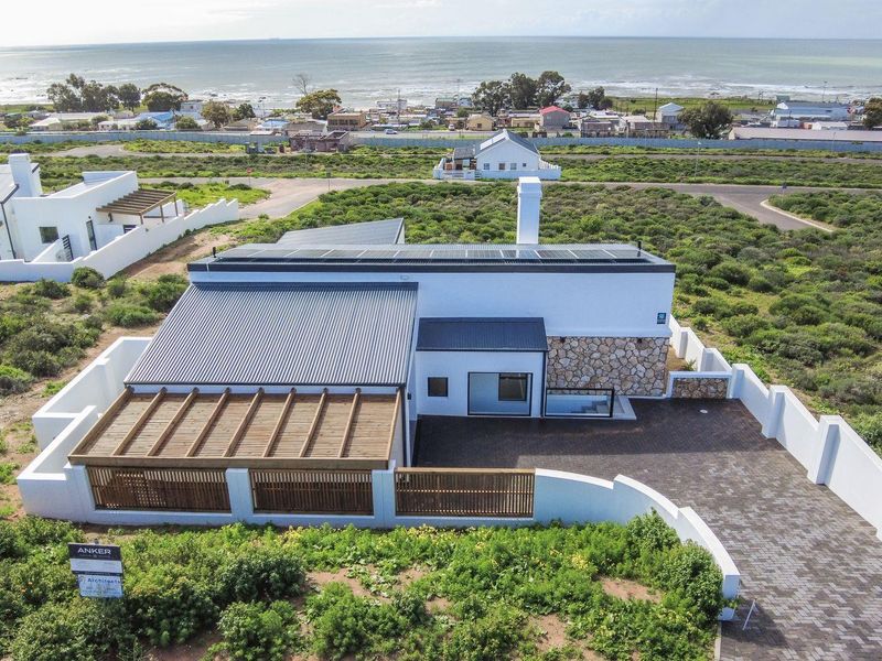 Aerial view of a modern coastal residence featuring a metal roof, solar panels, stone facade accents, and a timber pergola over the patio area.
