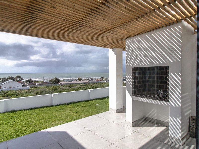 Covered patio featuring a timber slat pergola, built-in braai, and tiled flooring, offering expansive coastal views.