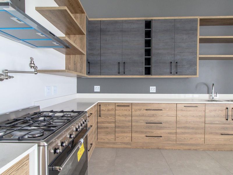 Modern kitchen featuring wood-grain cabinetry, dark grey upper cabinets, stone countertops, a gas stove with extractor, and a convenient pot filler faucet.