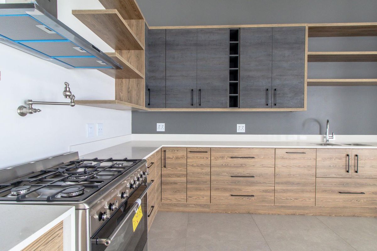 Modern kitchen featuring wood-grain cabinetry, dark grey upper cabinets, stone countertops, a gas stove with extractor, and a convenient pot filler faucet.