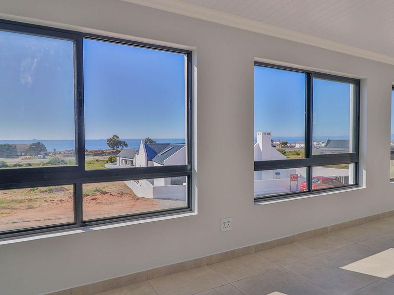 A bright, empty living area featuring large aluminium-framed windows that offer expansive coastal views and abundant natural light.