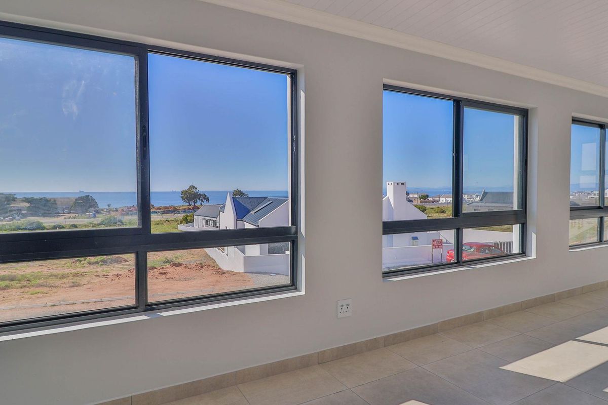 A bright, empty living area featuring large aluminium-framed windows that offer expansive coastal views and abundant natural light.