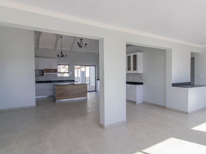Spacious open-plan living and kitchen area featuring modern cabinetry, stone countertops, a central island, and neutral tiled flooring throughout.