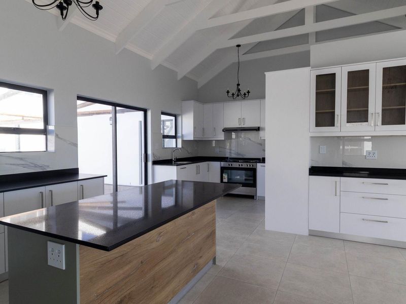 Modern, spacious kitchen featuring a large island, stone countertops, built-in appliances, and a high vaulted ceiling with exposed rafters.