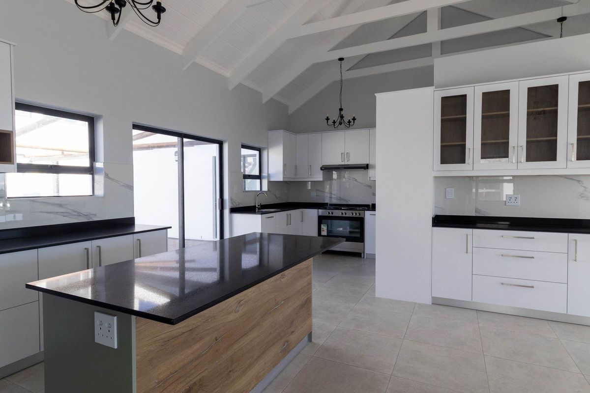 Modern, spacious kitchen featuring a large island, stone countertops, built-in appliances, and a high vaulted ceiling with exposed rafters.