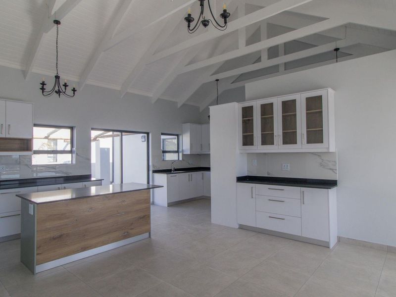 Spacious modern kitchen featuring a vaulted ceiling with exposed rafters, a central island, stone countertops, and ample white cabinetry with glass-front accents.