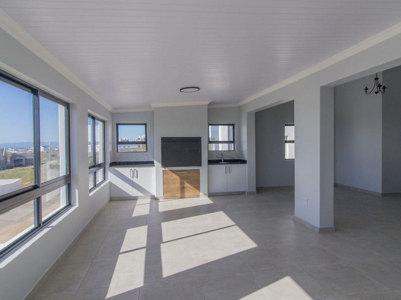 Spacious open-plan living area featuring tiled floors, built-in cabinetry with stone countertops, a built-in braai, and large windows providing ample natural light.