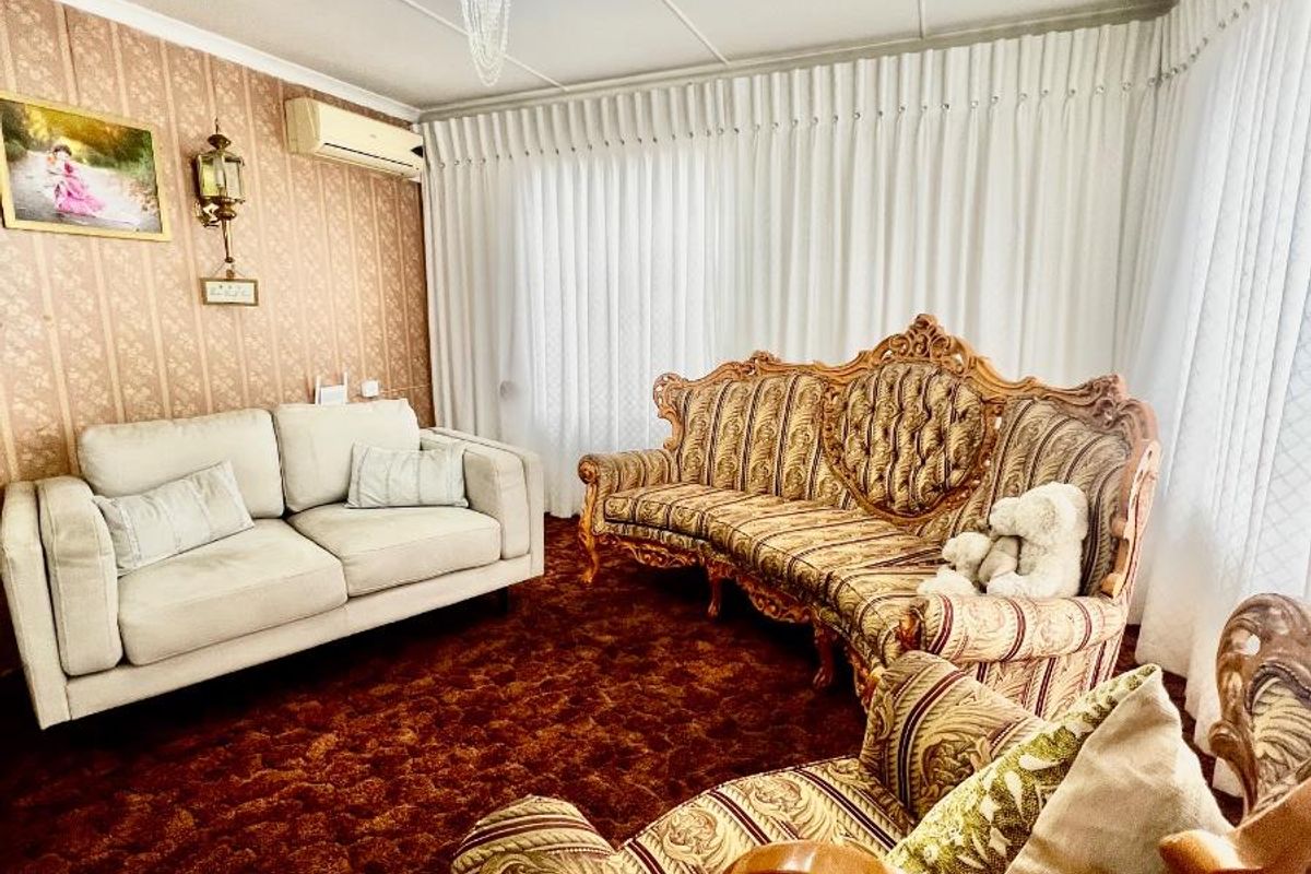 A traditional living room featuring patterned wallpaper, wall-mounted air conditioning unit, and a decorative crystal chandelier.