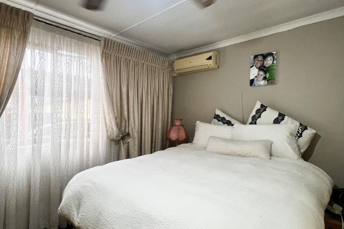 A bedroom featuring a wall-mounted air conditioning unit, a ceiling fan, and large windows with curtains.