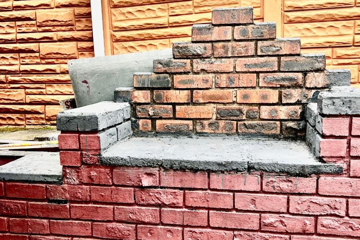A built-in brick braai or outdoor fireplace structure located in the rear garden area, featuring a masonry base and decorative brickwork.