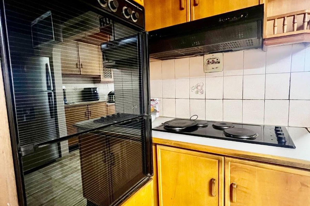 A dated kitchen featuring wooden cabinetry, a built-in oven, a black electric hob, and a tiled backsplash.