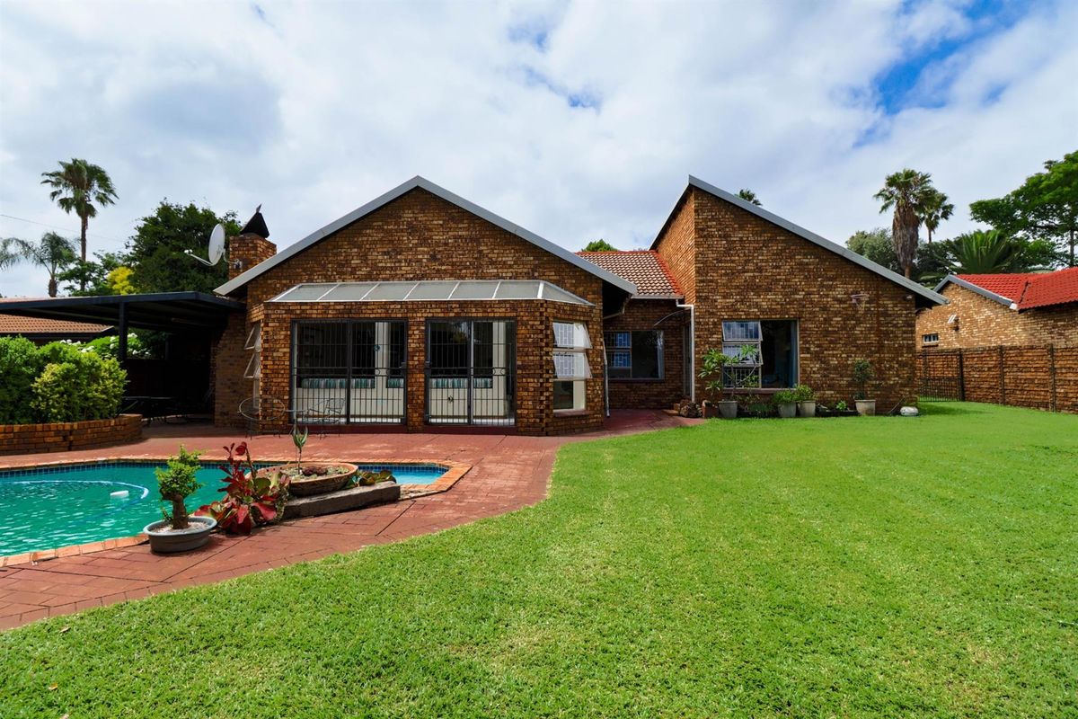 Rear view of the house featuring a face-brick facade, a swimming pool with paved surround, and a well-maintained lawn.