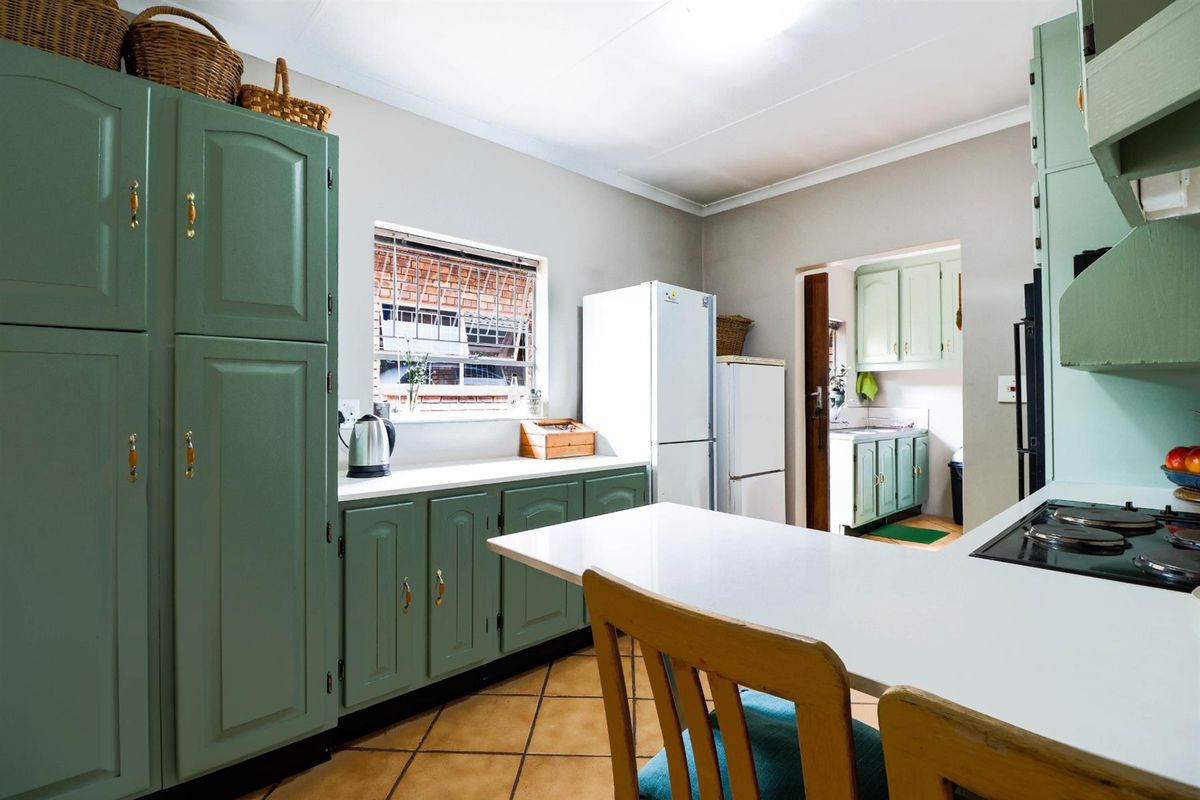 A functional kitchen featuring sage green cabinetry, white countertops, a built-in hob, and an adjoining scullery area with additional storage and workspace.