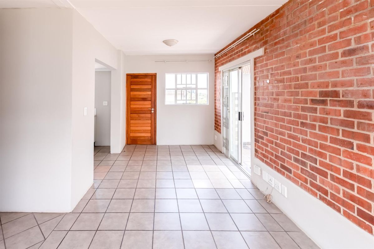 An empty living area featuring tiled floors, an exposed brick feature wall, and sliding glass doors providing access to the exterior.
