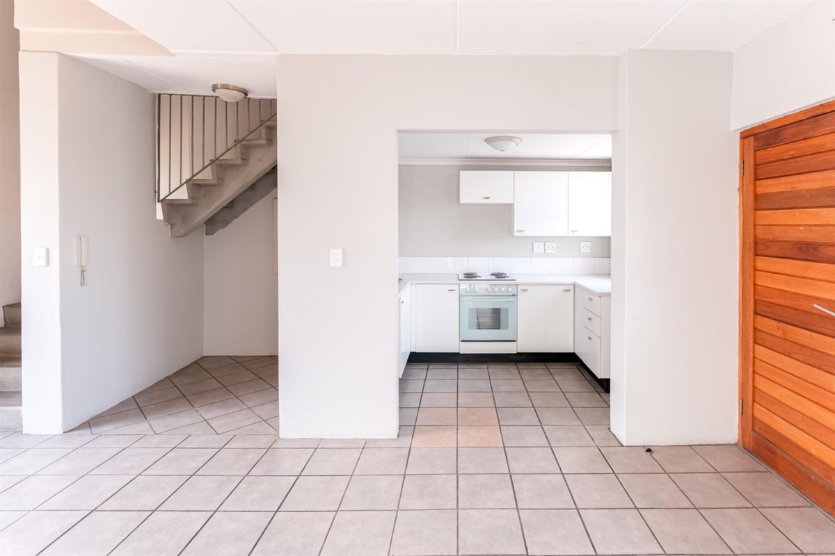 A functional kitchen area featuring white cabinetry, a stove, and tiled flooring, adjacent to an internal staircase and wooden door.