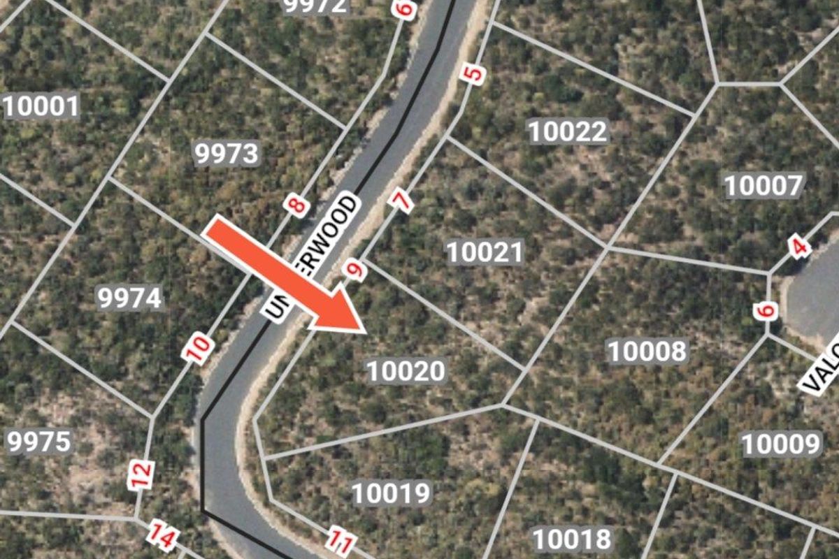 An aerial view of a residential vacant land plot, identified as lot 10020, situated within a developed estate with established road access.