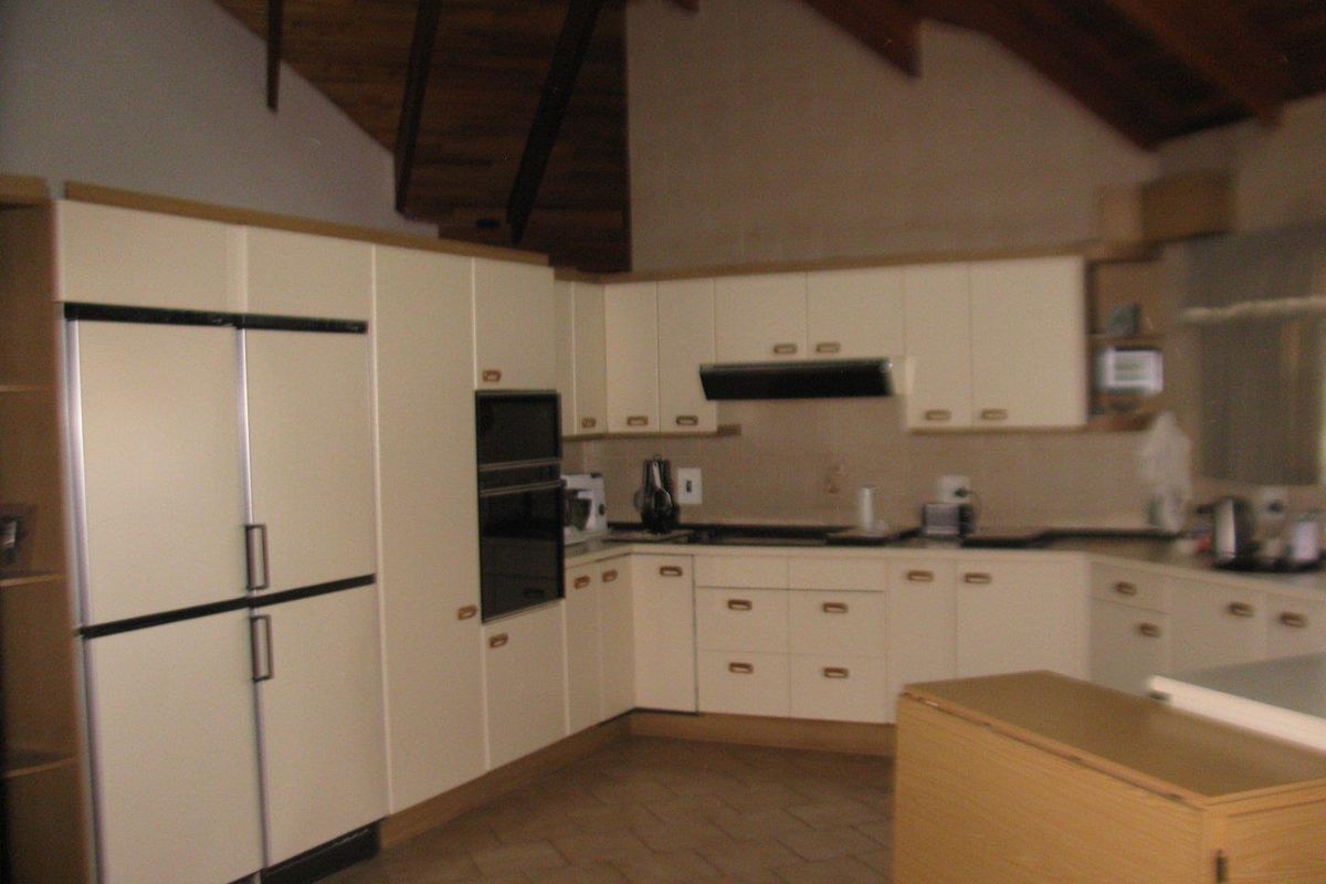 A functional kitchen featuring built-in cabinetry, integrated oven, extractor fan, and high vaulted timber ceilings in a farm-style property.