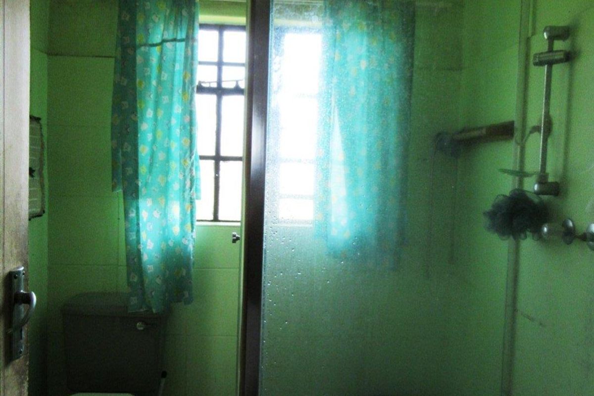 A functional bathroom featuring a glass-enclosed shower and a standard toilet, requiring cosmetic updates to modernize the space.