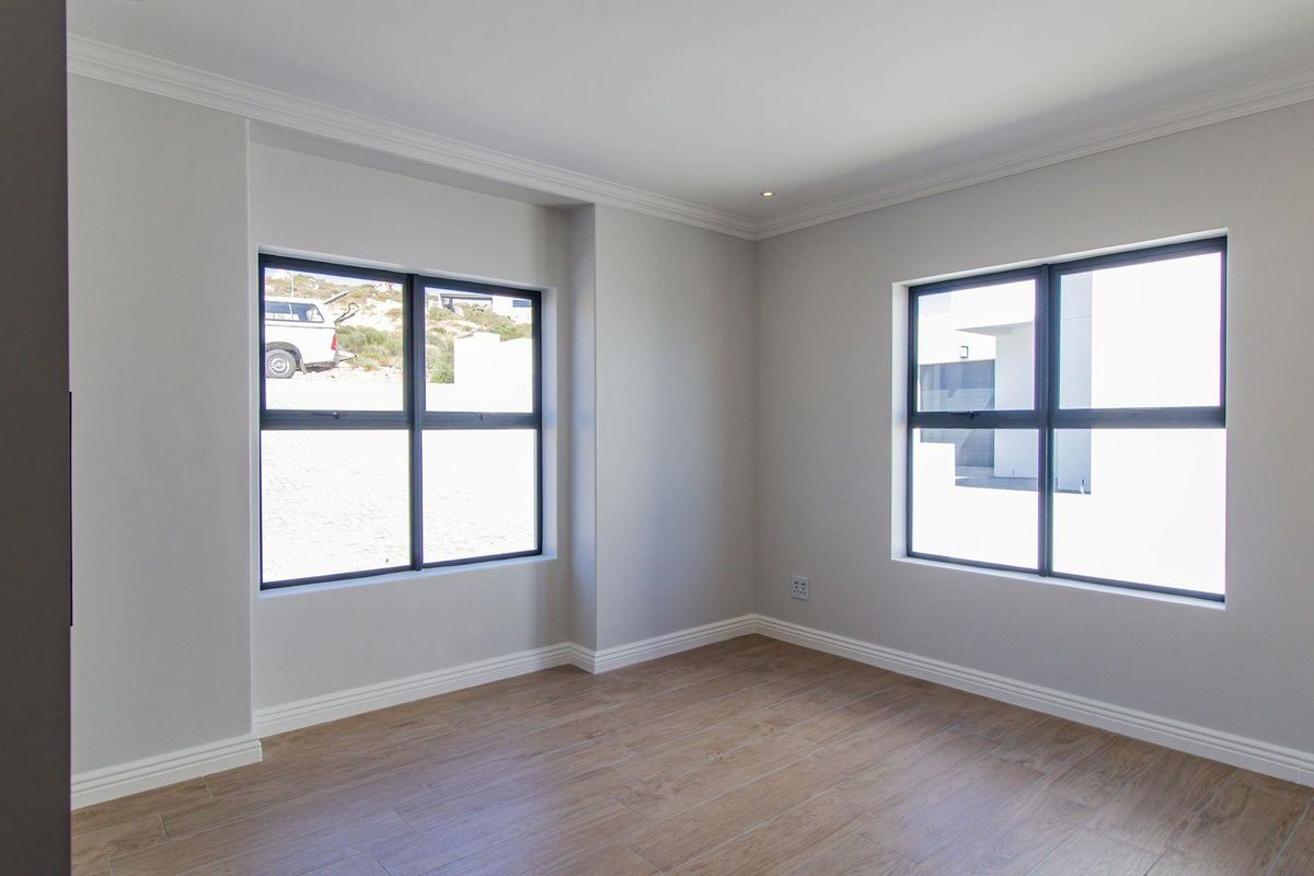 A bright, empty bedroom featuring modern wood-look tile flooring, neutral walls, crown molding, and dark-framed windows.