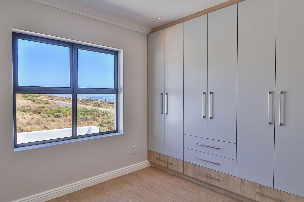A bright bedroom featuring modern built-in cabinetry with integrated drawers and a large window offering scenic coastal views.