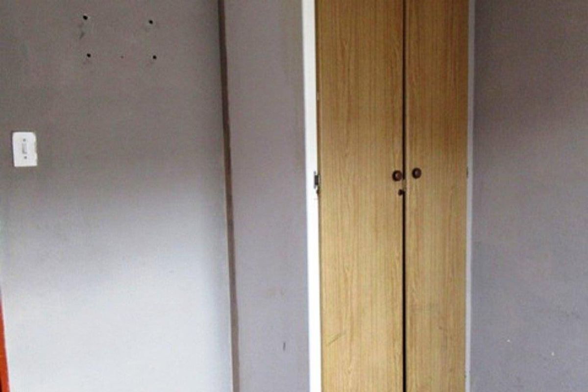 A bedroom corner featuring a built-in wooden wardrobe, red carpeting, and grey painted walls with visible wear and tear.