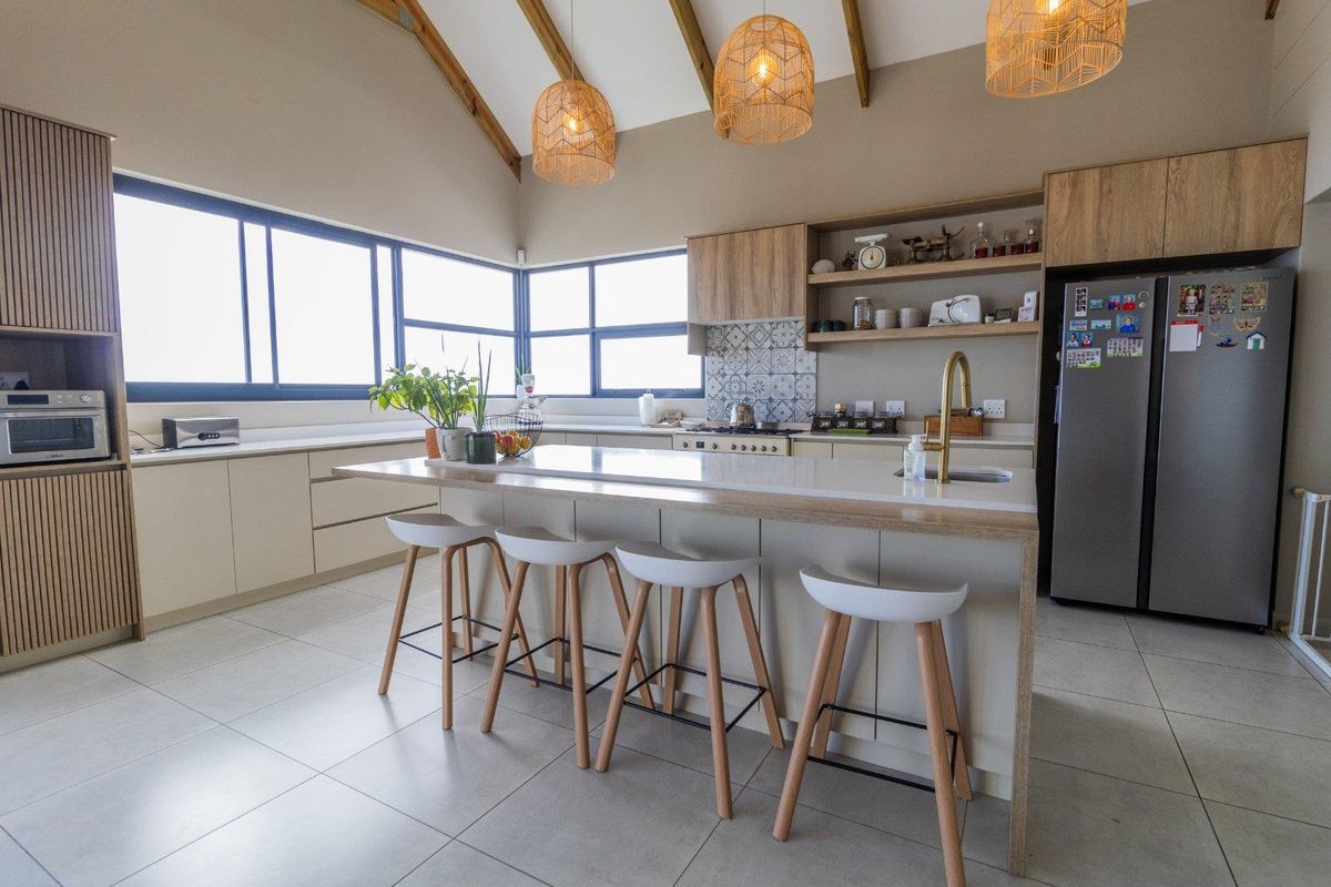 Modern kitchen featuring a central island with breakfast bar, stone countertops, timber cabinetry, vaulted ceilings with exposed beams, and large windows for natural light.