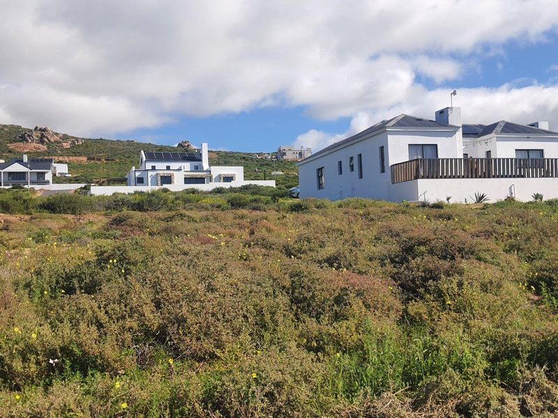 A view of a residential property featuring a white exterior, solar panels, and a timber deck, set against a natural fynbos landscape.