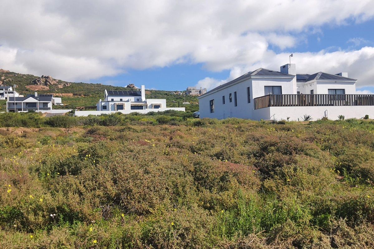A view of a residential property featuring a white exterior, solar panels, and a timber deck, set against a natural fynbos landscape.