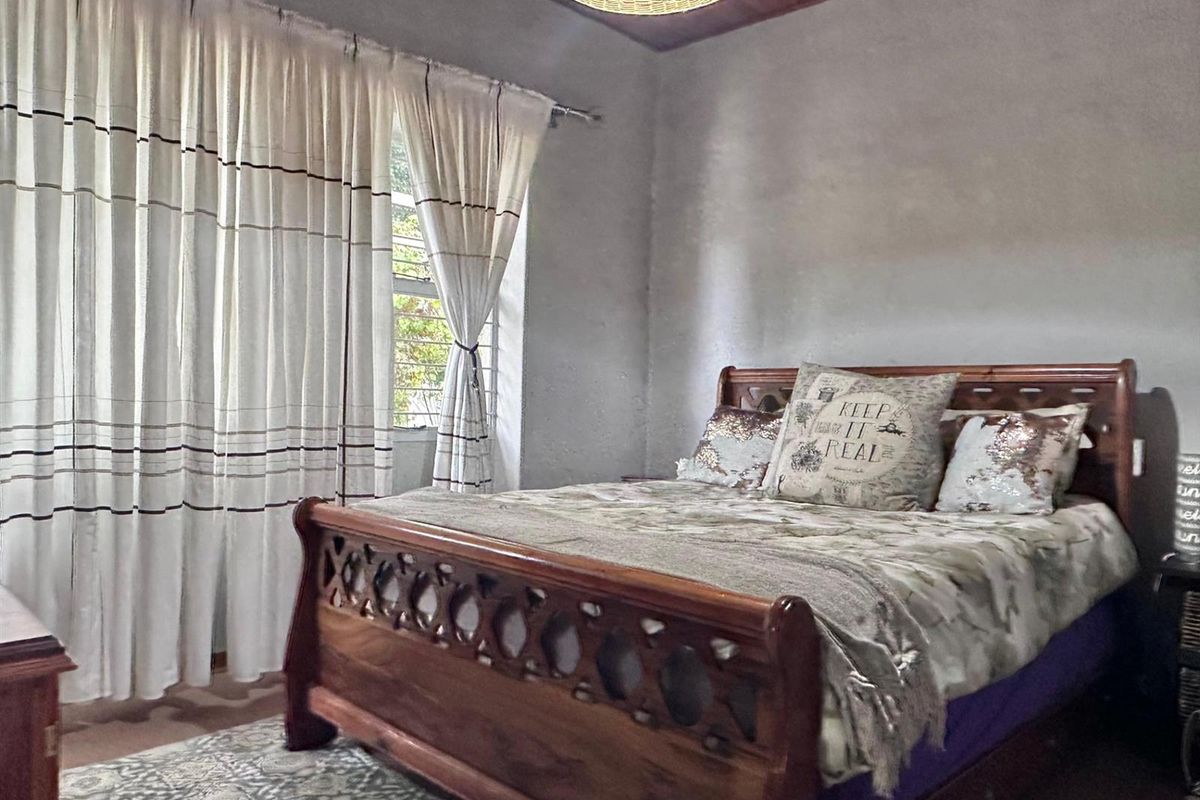 A bedroom featuring a timber-paneled ceiling, large window with curtains, and neutral wall finishes.
