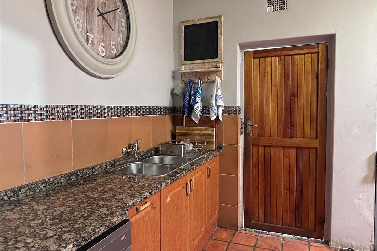 A functional kitchen area featuring granite countertops, a double stainless steel sink, tiled splashbacks, and a solid timber door leading outdoors.
