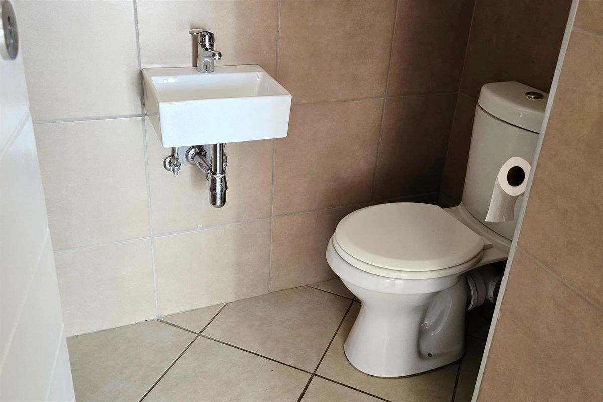 A compact guest bathroom featuring a wall-mounted basin and a standard toilet with neutral floor and wall tiling.