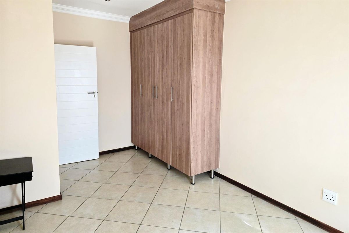 A bedroom featuring neutral wall tones, tiled flooring, and a large built-in wooden wardrobe with modern metal handles.