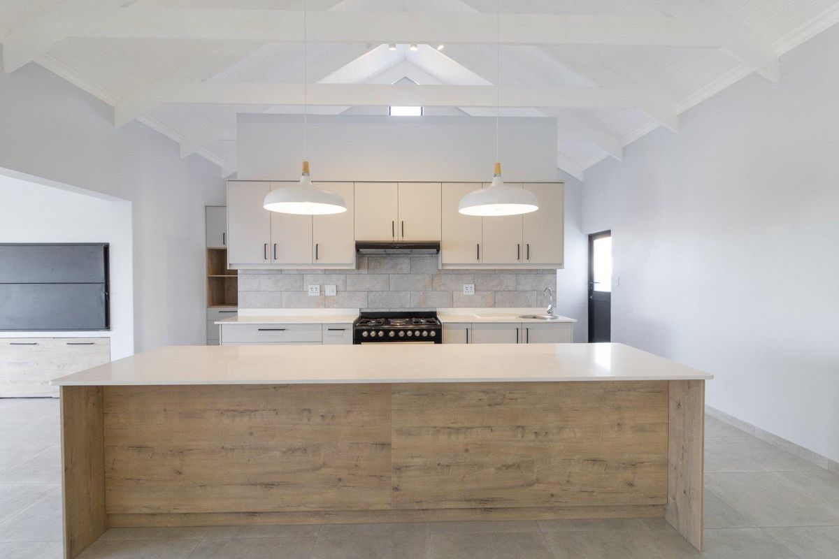 Modern kitchen featuring a large central island, stone countertops, built-in gas stove, extractor fan, and vaulted ceilings with exposed beams.