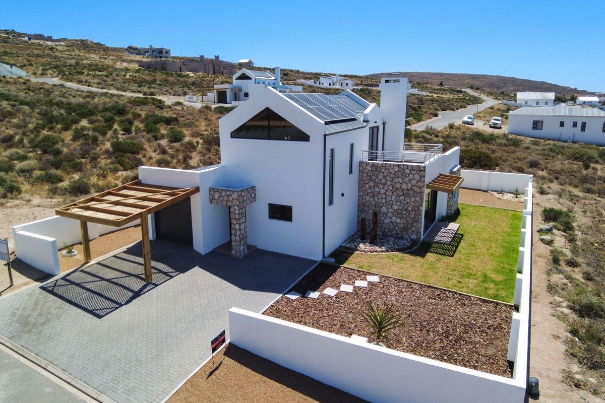 Aerial view of a modern white house featuring solar panels, stone cladding accents, a paved driveway, wooden pergola, and a landscaped garden.